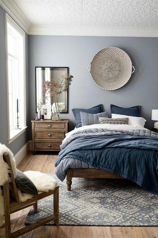 a chic blue bedroom with stained wooden furniture, a woven basket on the wall, blue bedding, a mirror, a boho rug and some faux fur