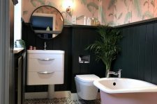 a chic tropical bathroom with tropical wallpaper, black panels, a pink tub, a floating vanity and a lamp with fringe