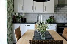 a chic vintage-inspired kitchen with tropical wallpaper, white cabinets and subway tiles, wooden furniture and woven chairs