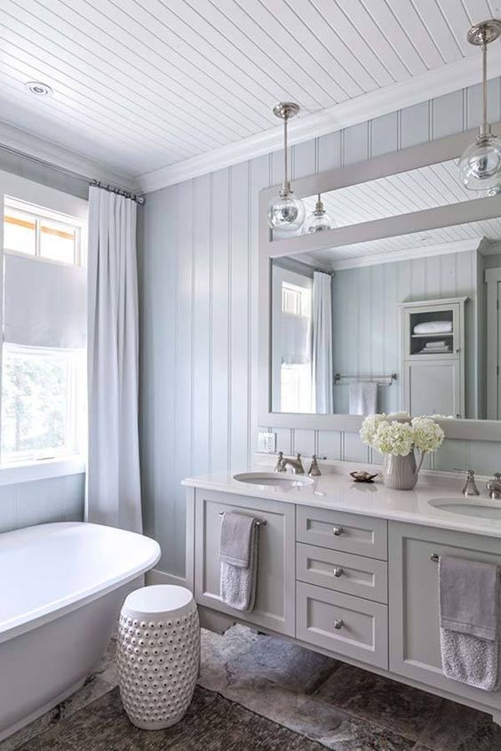 a classic beach bathroom done with blue shiplap, a tub, a floating grey vanity, a mirror ina  frame and pendant lamps