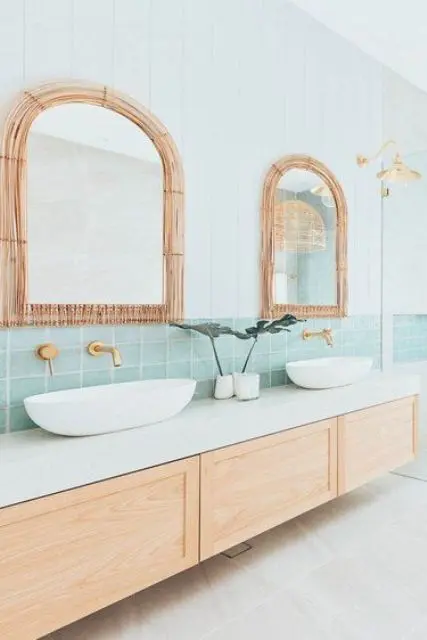 a coastal bathroom clad with shiplap and mint green tiles, a floating vanity, arched mirrors with rattan frames