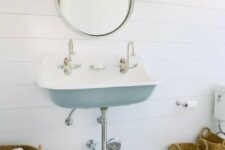 a coastal bathroom done with white shiplap, with a wall-mounted vanity, some baskets, a printed rug and a round mirror
