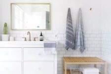 a coastal bathroom done with white subway and blue graphic tiles, a white vanity, a wooden bench, some towels and potted plants