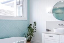 a coastal bathroom with blue herringbone and white marble tiles, a shiplap wall, a white vanity and an oval tub, a side table