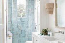 a coastal bathroom with blue tiles in the shower, a white vanity and white tiles, a mirror and some wall sconces