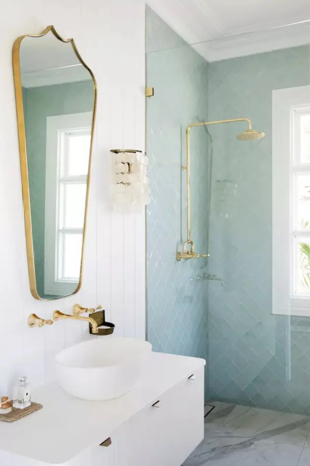 a coastal bathroom with mint blue tiles and white marble ones, a white floating vanity, a mirror and gold fixtures