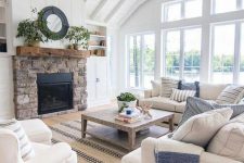 a coastal farmhouse living room in white, with tan and creamy furniture, printed pillows, a brick clad fireplace, a chandelier and a striped rug