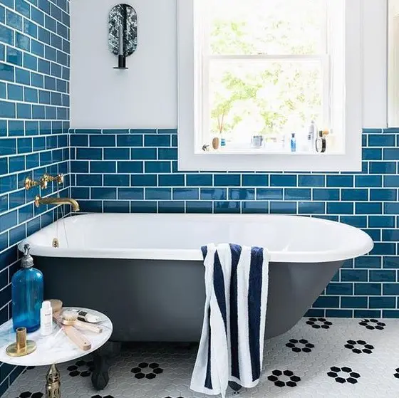 a coastal-inspired bathroom with navy subway tiles, a black bathtub and some cute accessories