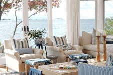 a coastal living room with glazed walls, neutral and striped blue furniture, a wooden table, candleholders and baskets