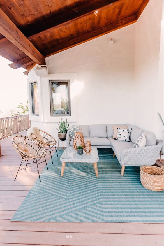 a coastal porch with a grey L-shaped sofa, a glass table, rattan chairs and potted plants is stylish and welcoming