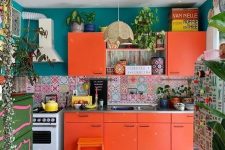 a colorful kitchen with orange cabinets, a mosaic tile floor and a colorful backsplash, teal walls and lots of plants