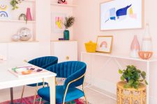 a colorful mid-century modern home office with pale pink walls, a colorful rug, bold blue chairs and artworks and accessories