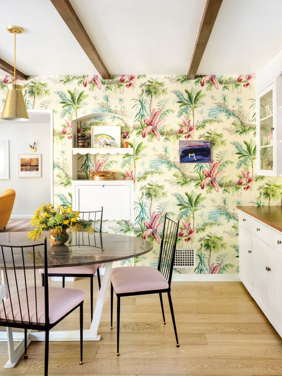 a colorful tropical kitchen with bright printed wallpaper, white cabinets, a round table and pink chairs is fun and cool
