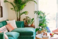 a colorful tropical living room with an emerald sofa, a colorful boho rug, potted plants and a round wooden table