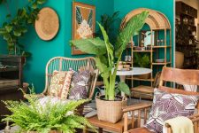 a colorful tropical living room with emerald walls, rattan and leather furniture, a gold mirror, potted plants and bold artworks