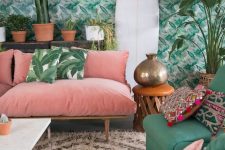 a colorful tropical living space with a tropical print wall, a pink sofa and emerald chairs, tropical pillows and lots of plants