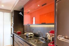 a contemporary dark kitchen spruced up with bold orange sleek upper cabinets and lights looks dramatic