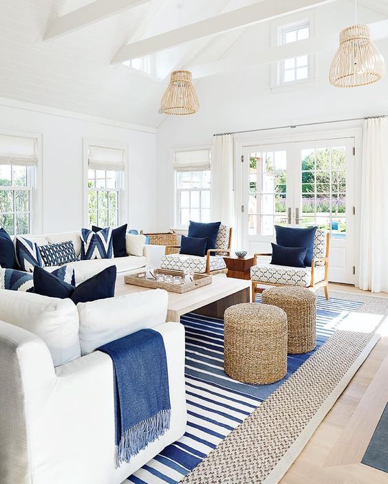 a contrasting coastal living room in white, with creamy furniture, navy pillows and blankets, woven ottomans and rattan lamps
