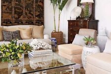 a contrasting tropical living room with white walls, neutral furniture, a dark artwork and sideboard and tropical plants