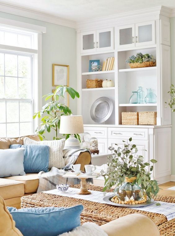 a cozy coastal living room in neutrals, with tan furniture, white and blue pillows, greenery and baskets