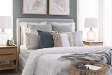 a cozy grey bedroom with grey walls, a dove grey bed and ottoman, layered rugs, light-stained wood