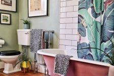 a cute tropical bathroom with green walls, white subway tiles, a pink clawfoot tub, a banana leaf curtain and potted greenery