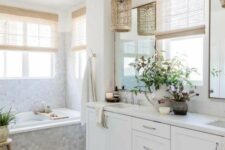 a delicate coastal bathroom with a pale blue tile bathtub, a white vanity, shades and woven pendant lamps and a printed rug