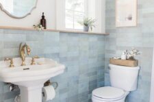 a delicate coastal bathroom with blue skinny tiles and printed ones, white appliances, some art and greenery