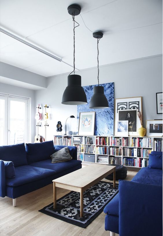 a dove grey living room with navy sofas and a matching artwork, a long booksehfl an a printed rug