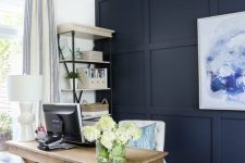 a farmhouse home office with a navy paneled accent wall, a wooden trestle desk, a storage unit and a basket for storage