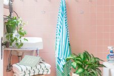 a fun tropical bathroom with pink tiles, a black edge, potted plants and striped towels looks cute