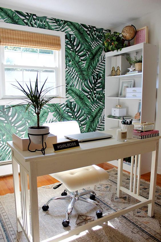 a fun tropical home office with a tropical leaf wall, woven shades, a white leather chair and potted plants