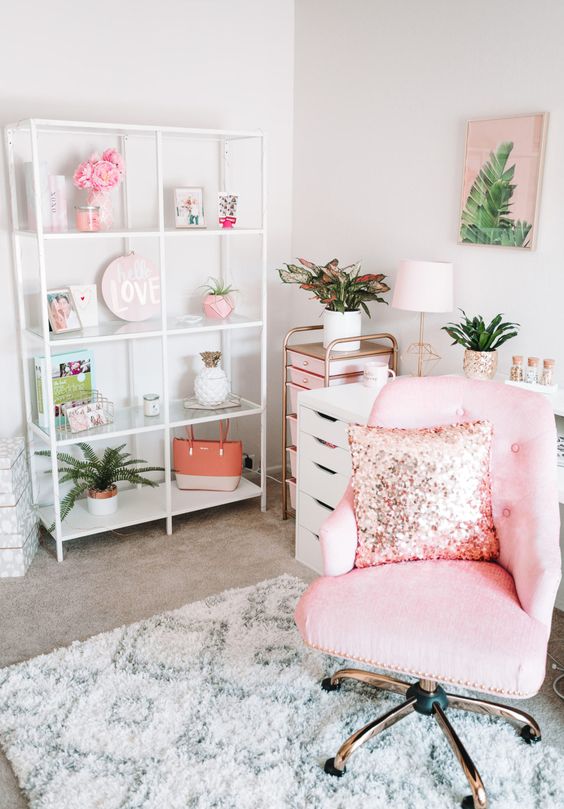 a glam tropical home office with a pink chair with a sequin pillow, a pink storage unit, tropical leaf artworks and a storage unit with pink accessories