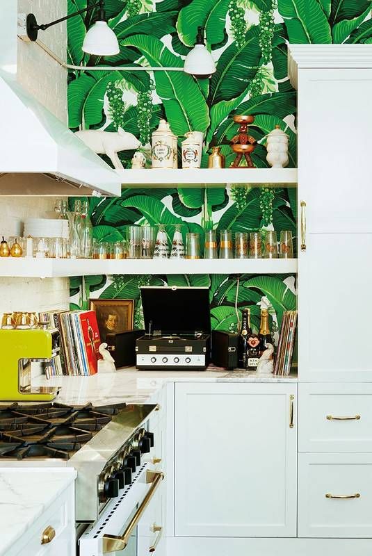 a glam tropical kitchen with banana leaf wallpaper, white cabinets, gold handles and wall sconces for a chic look