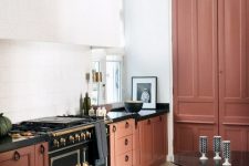 a gorgeous burnt orange kitchen with a refined black cooker and black stone countertops plus colorful stools