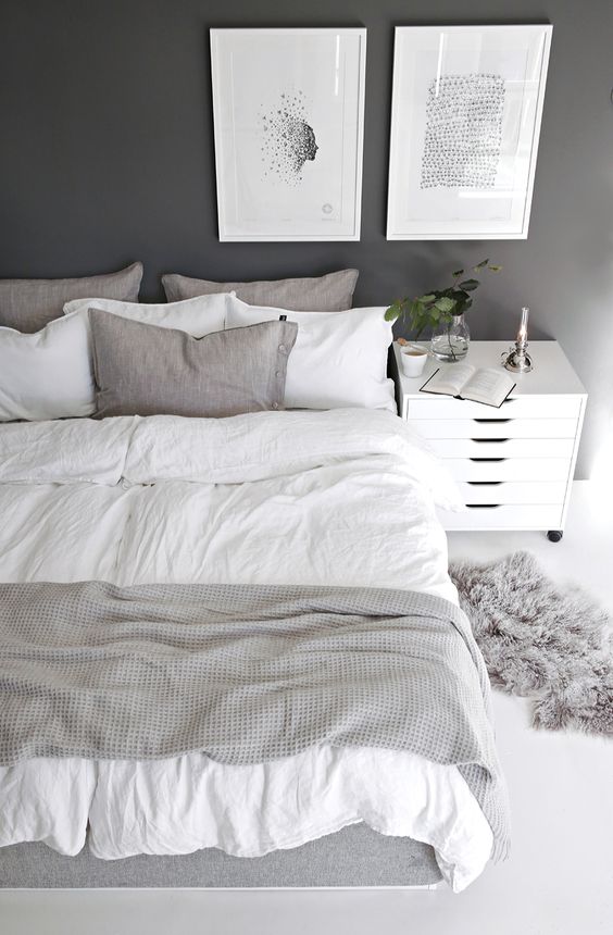 a grey Nordic bedroom with a graphite grey wall, grey and white bedding and a fur rug, a chic gallery wall