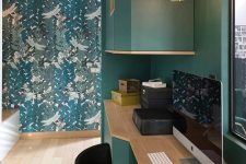 a home office space with a hunter green wall and furniture, a botanical print wall, wooden furniture and geometric pendant lamps