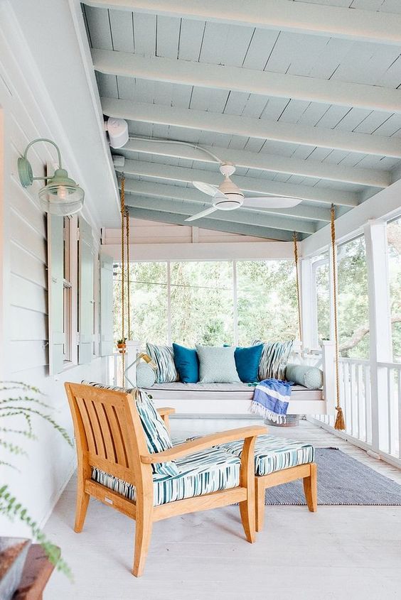 a lovely coastal porch with a hanging daybed and a lounger styled with blue printed pillows and upholstery