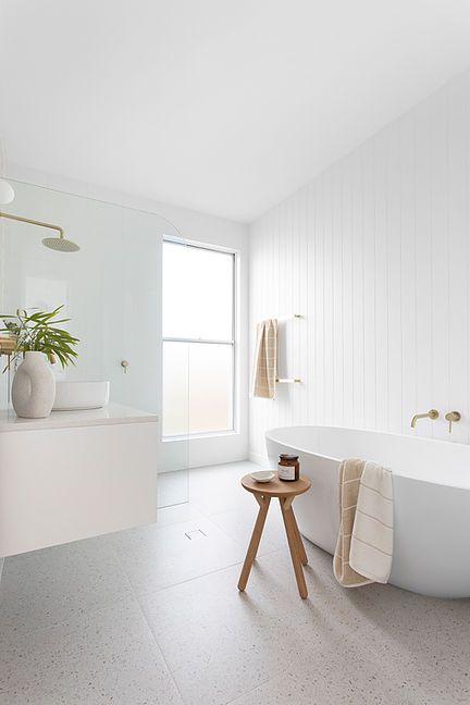 a minimalist beach bathroom with white shiplap and grey terrazzo tiles, a floating vanity, an oval tub and a wooden stool