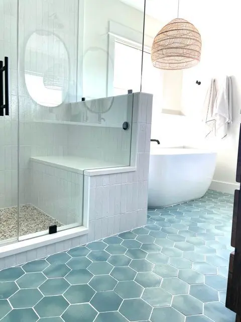 a modern coastal bathroom done with blue hex tiles, a shower space clad with white skinny ones, a tub and a woven pendant lamp