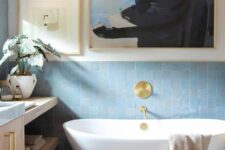 a modern coastal bathroom with blue zellige tiles, a large timber vanity, an oval tub, a pretty gallery wall and a fluffy rug