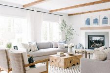 a modern coastal farmhouse living room with grey furniture, a wooden table, wicker stools and white chairs plus blue artworks