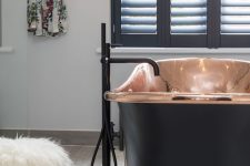 a modern luxurious bathroom with a copper and black bathtub for a statement, black shutters and black fixtures