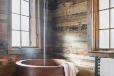 a modern rustic bathroom clad with weathered wood, with a copper Japanese soaking tub and wooden furniture