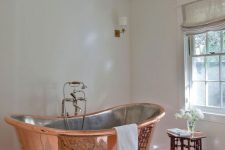 a modern sophisticated bathroom in neutrals, with a copper bathtub, a catchy stool, lamp and rug