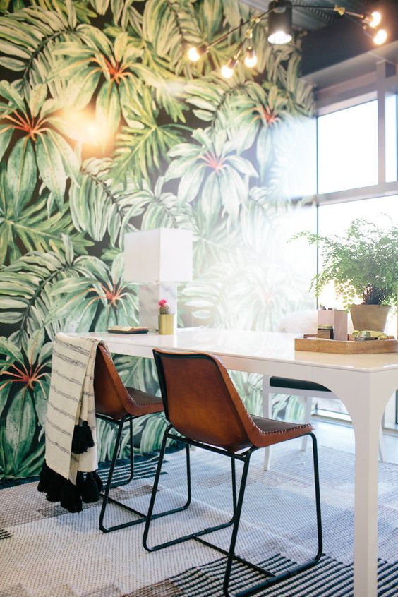 a moody home office with a statement tropical wall, a white desk, leather chairs and some potted greenery is lovely