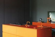 a moody kitchen in black and dark green, with orange cabinets and a kitchen island plus bright orange fixtures