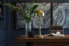 a moody navy home office with built-ins, a heavy wooden desk, a leather chair and touches of gold plus a cool gallery wall