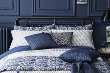 a moody refined bedroom with navy paneling, a black metal bed, vintage stools and navy bedding