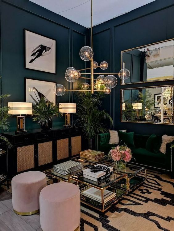 a moody tropical living room with teal walls, an emerald sofa, pink ottomans, a black sideboard and touches of gold